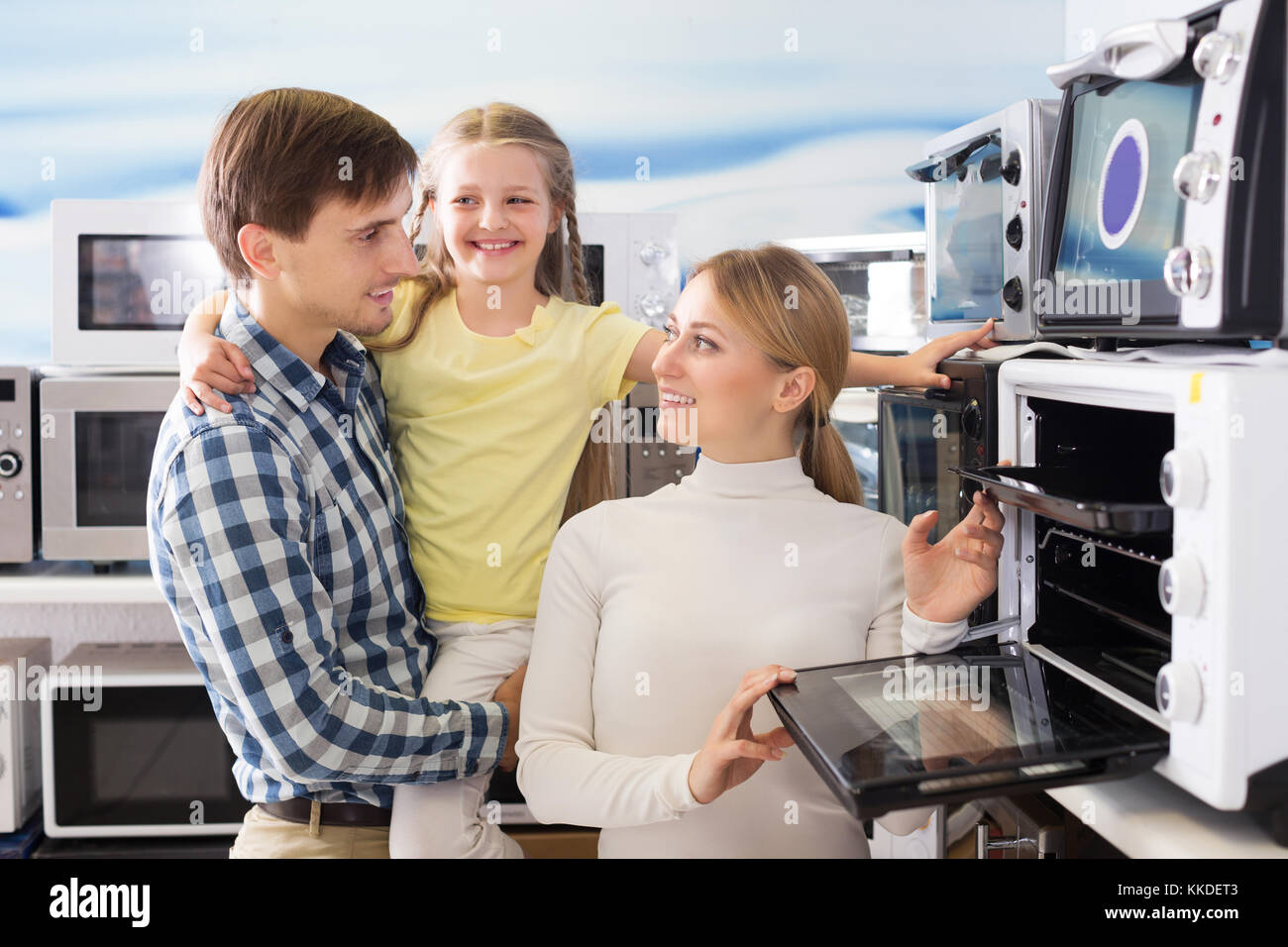 Smiling man and woman with girl buying modern microwave in store with electronics Stock Photo