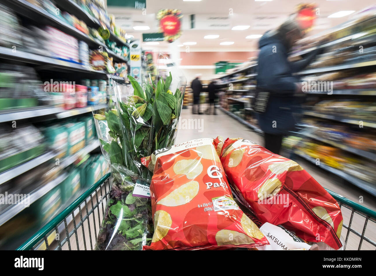 A shopping trolley full of goods being pushed down an aisle in a supermarket. Stock Photo