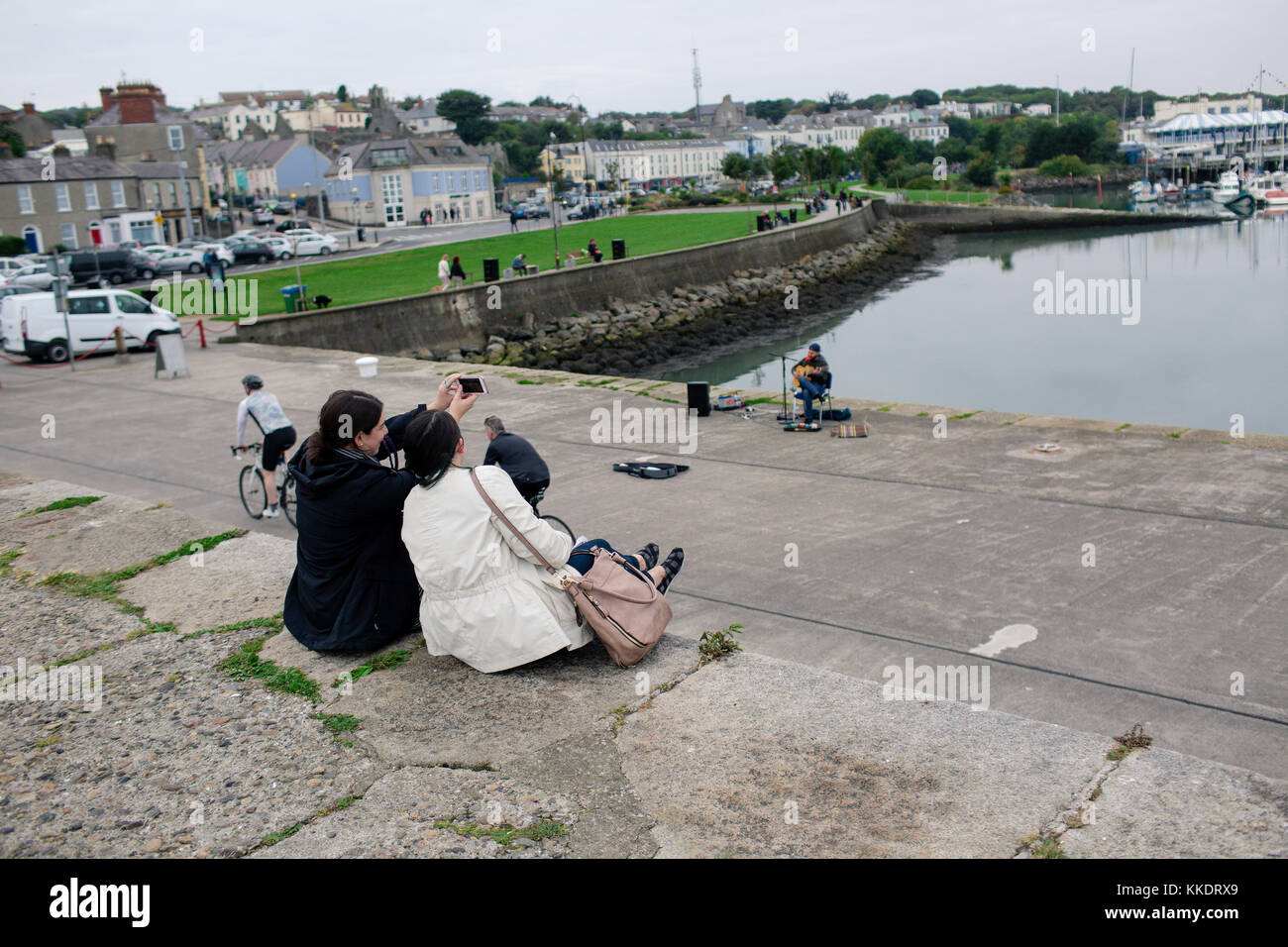 Tourists sitting on the Howth harbor pier making memories enjoying the view and taking selfies. Howth Peninsula, Dublin, Ireland Stock Photo