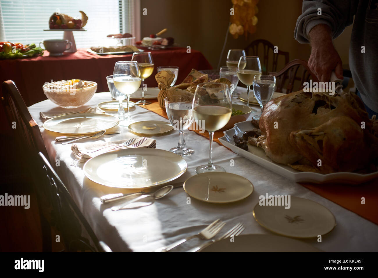 Man carving a turkey at a Thanksgiving table set with formal dinnerware