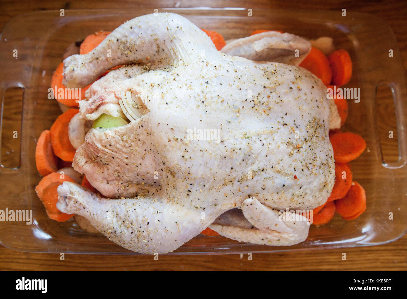 An overhead shot of seasoned, uncooked chicken pieces arranged on a bed of carrots in a casserole dish, ready for roasting. Meal prep concept. Stock Photo