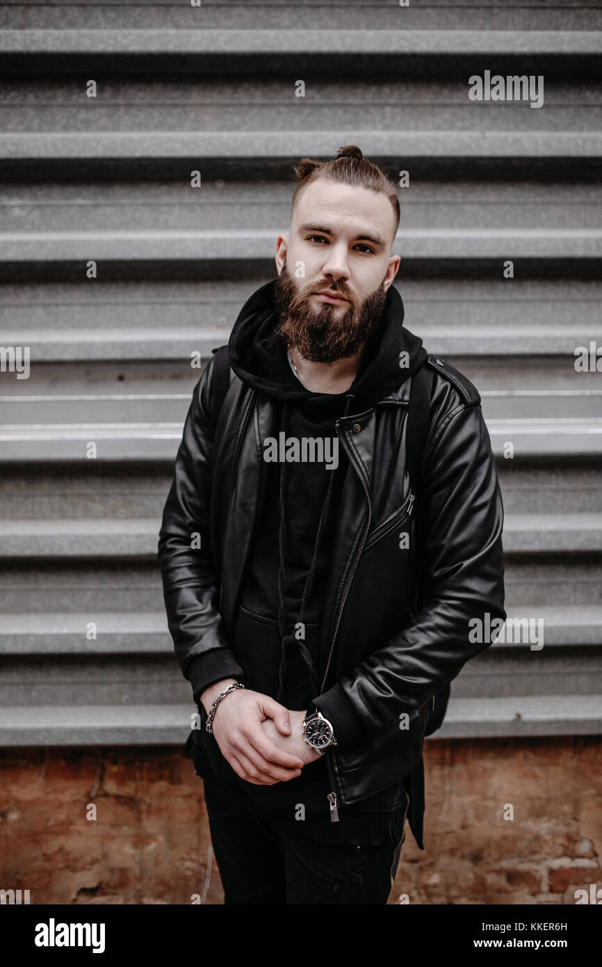 Modern young bearded man in black style clothes standing in around urban background. Stock Photo
