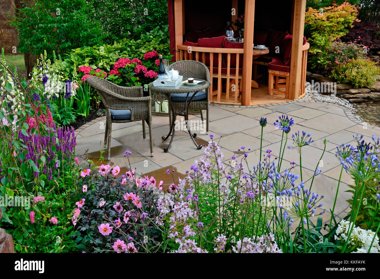 The patio area in a aquatic garden with colourful flower border and attractive seating Stock Photo