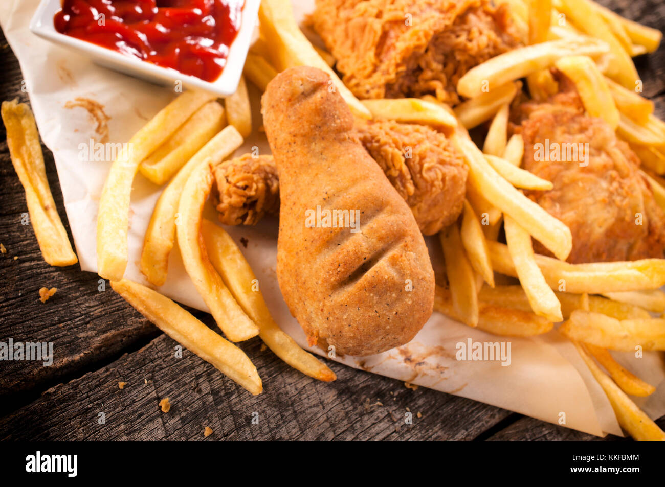 French fries and chicken legs on the wooden table.Selective focus on fried chicken leg in the middle Stock Photo