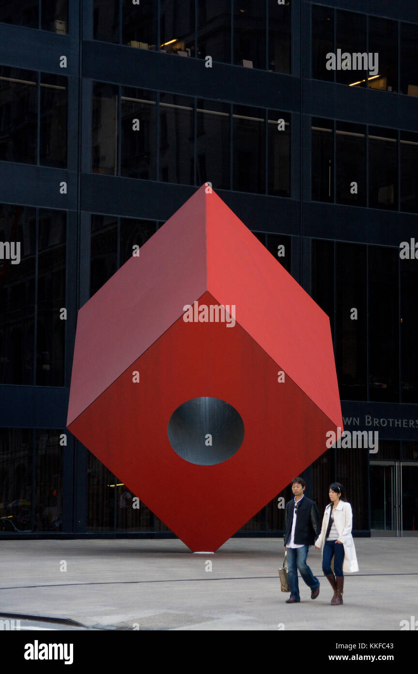 A couple strolls by Red Cube, a 1968 sculpture by Isamu Noguchi which sits on Broadway, between Liberty and Cedar streets in New York's financial dist Stock Photo
