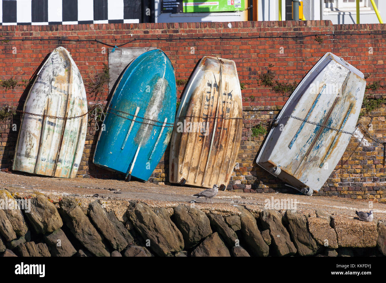 A row of rowing boats propped up against a brick wall at the folkestone