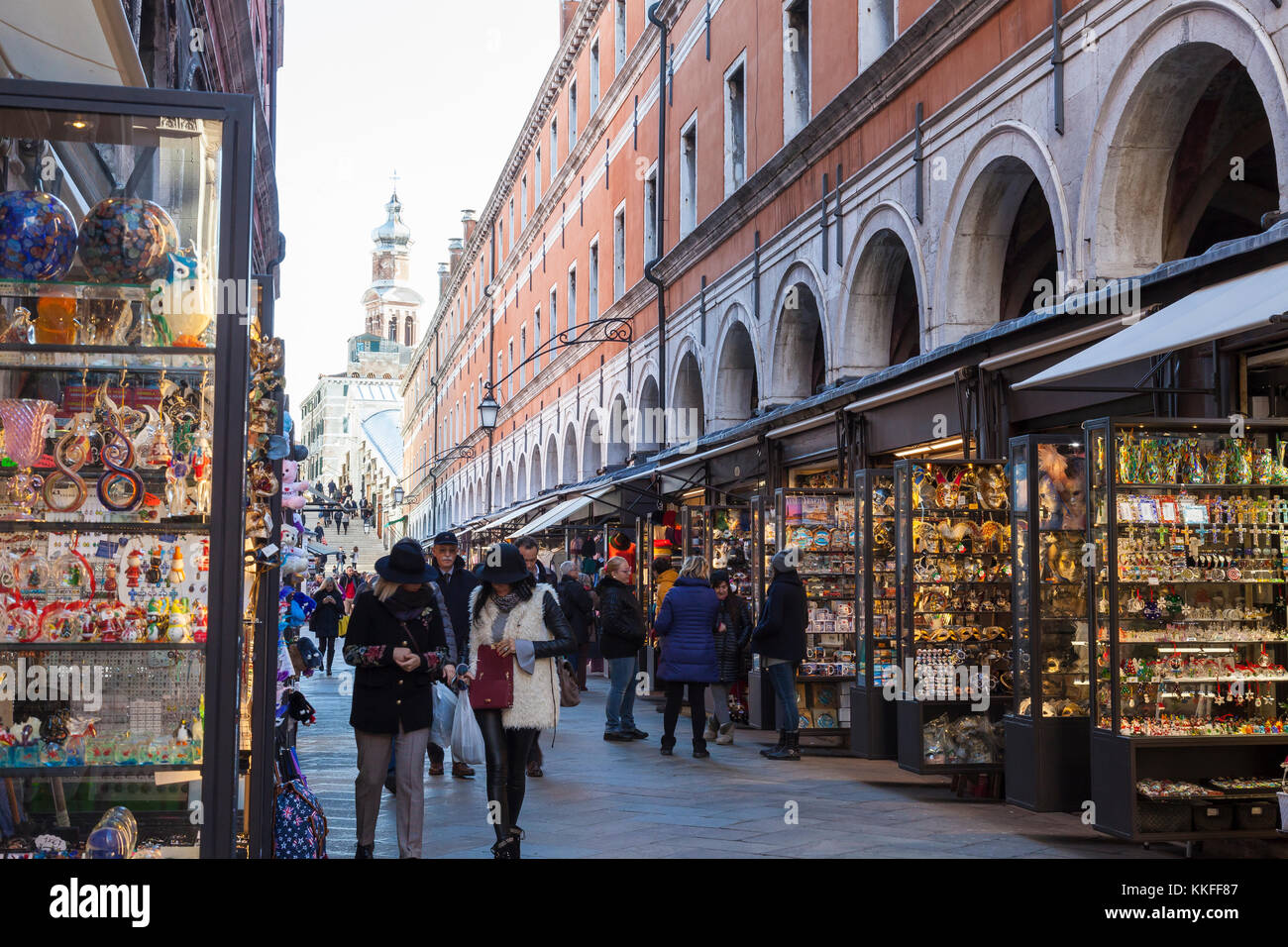 People shopping in brightly lit kiosks in Rialto Mercato, Venice, Italy on a cold autumn morning looking back to Rialto Bridge Stock Photo