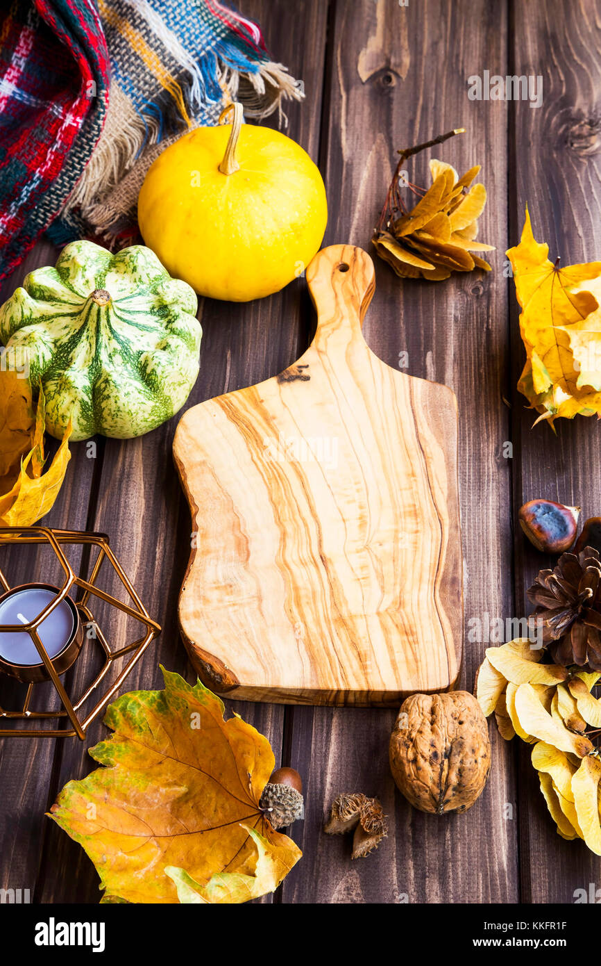 Autumn setting with wooden cutting board copy space, dried leaves , nuts and pumpkins, top view Stock Photo