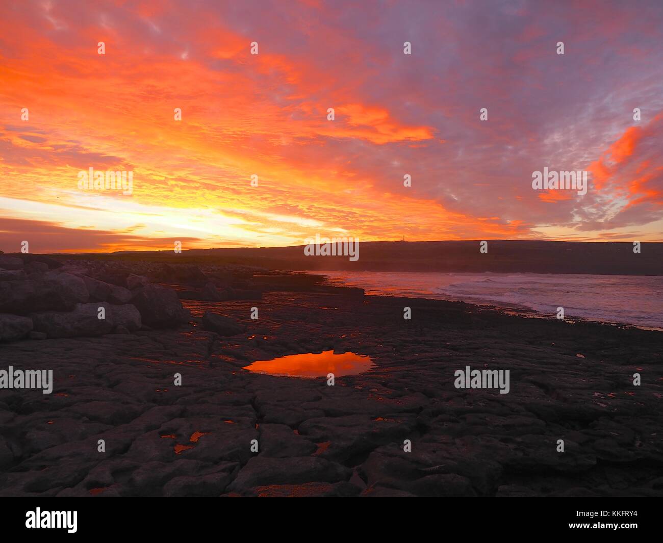 The sun rises over the Wild Atlantic Way at Doolin Pier, County Clare, Ireland turning the rock pools a sunburst red. Stock Photo