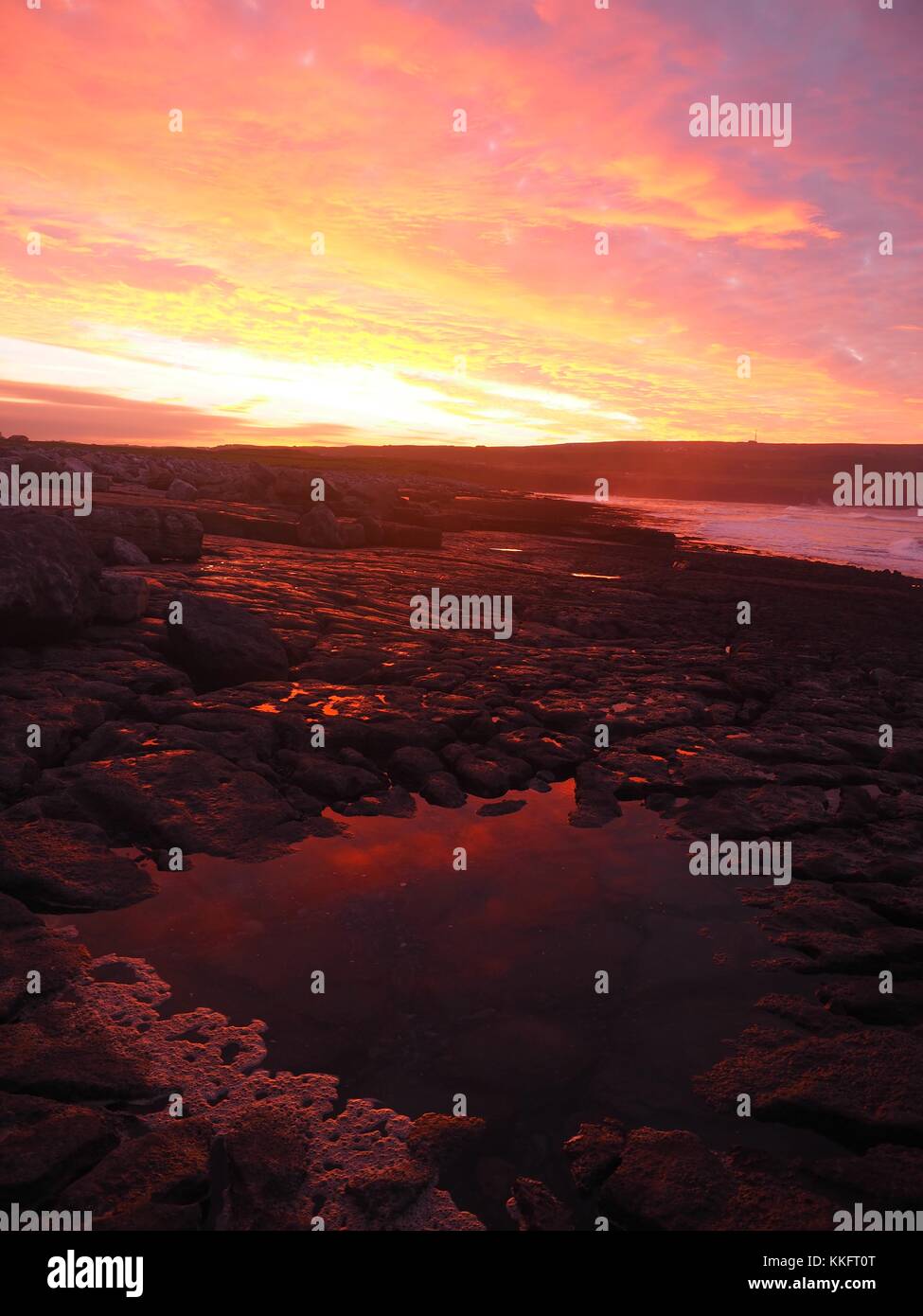 The sun rises over the Wild Atlantic Way at Doolin Pier, County Clare, Ireland turning the rock pools a sunburst red. Stock Photo