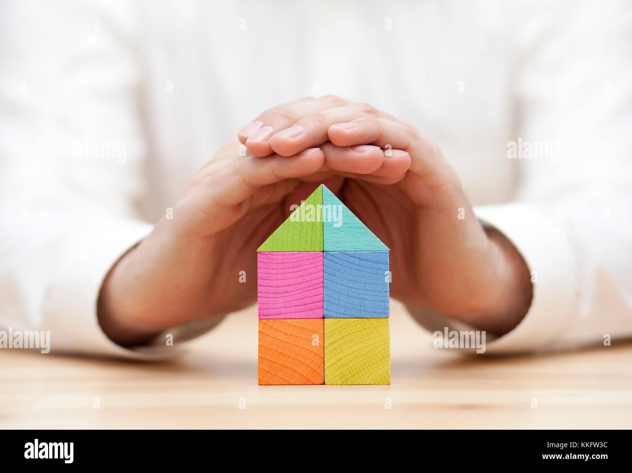 Colorful wooden block house protected by hands Stock Photo