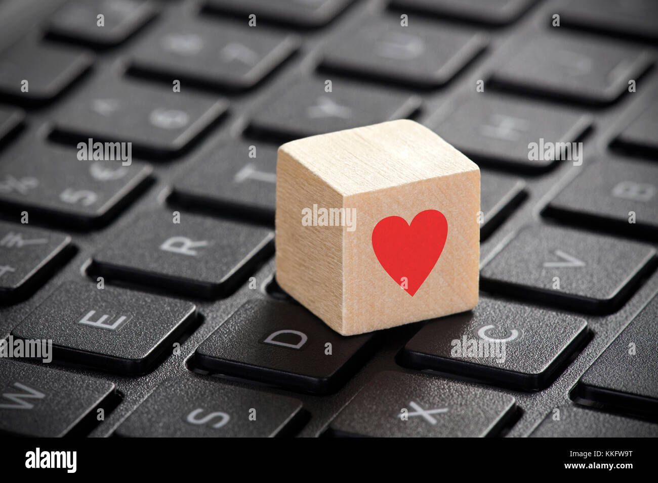 Wooden block with red heart shape on laptop keyboard. Stock Photo