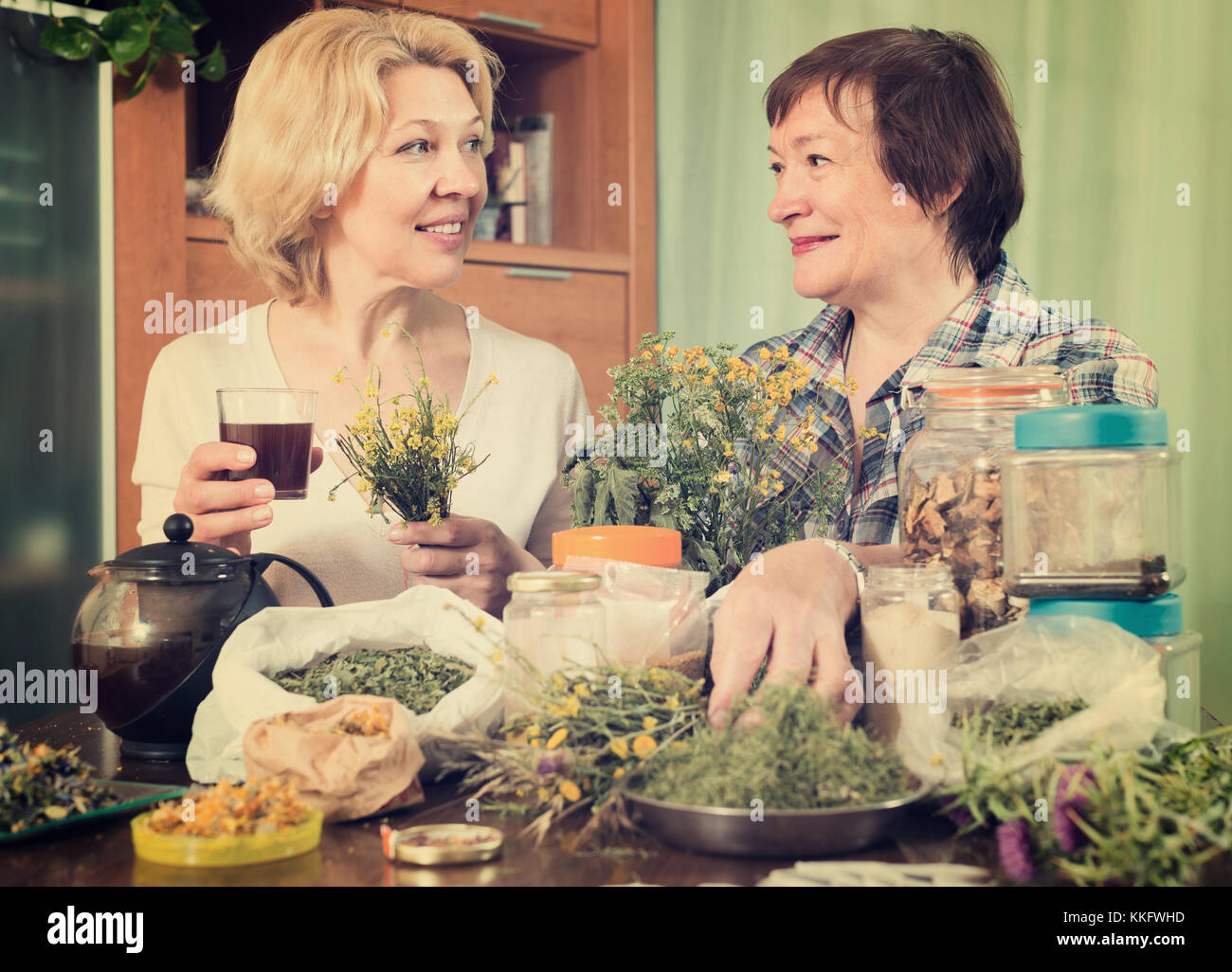 Two senior women sitting at the table and brewing herbal tea with ...