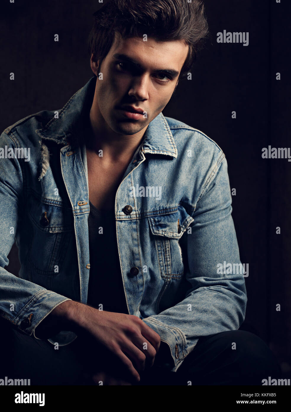 Handsome male model posing in fashion blue jeans jacket looking on dark  shadow background. Closeup toned portrait Stock Photo - Alamy