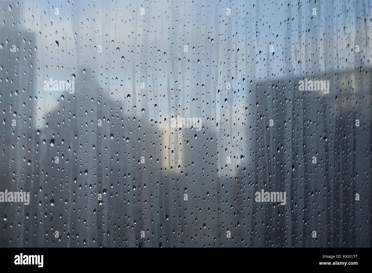 close-up of water droplets on window with buildings and blue sky and clouds in background Stock Photo