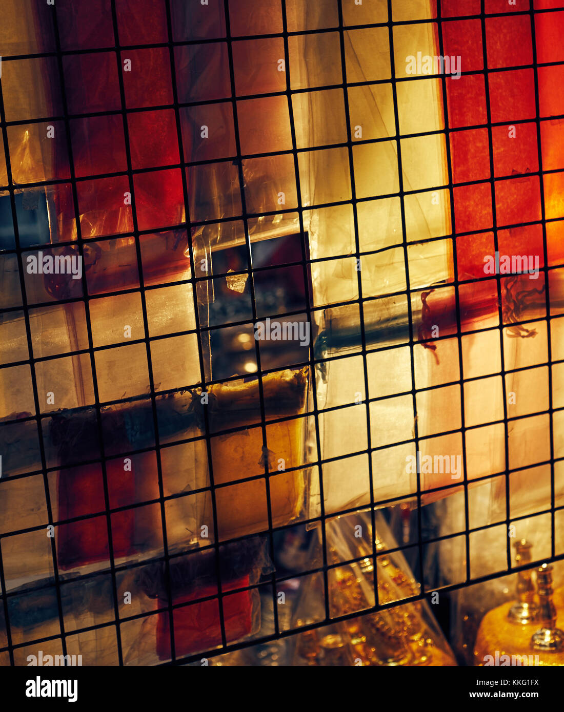 soft light glowing through closed market window that is covered in chicken wire and colored plastic Stock Photo