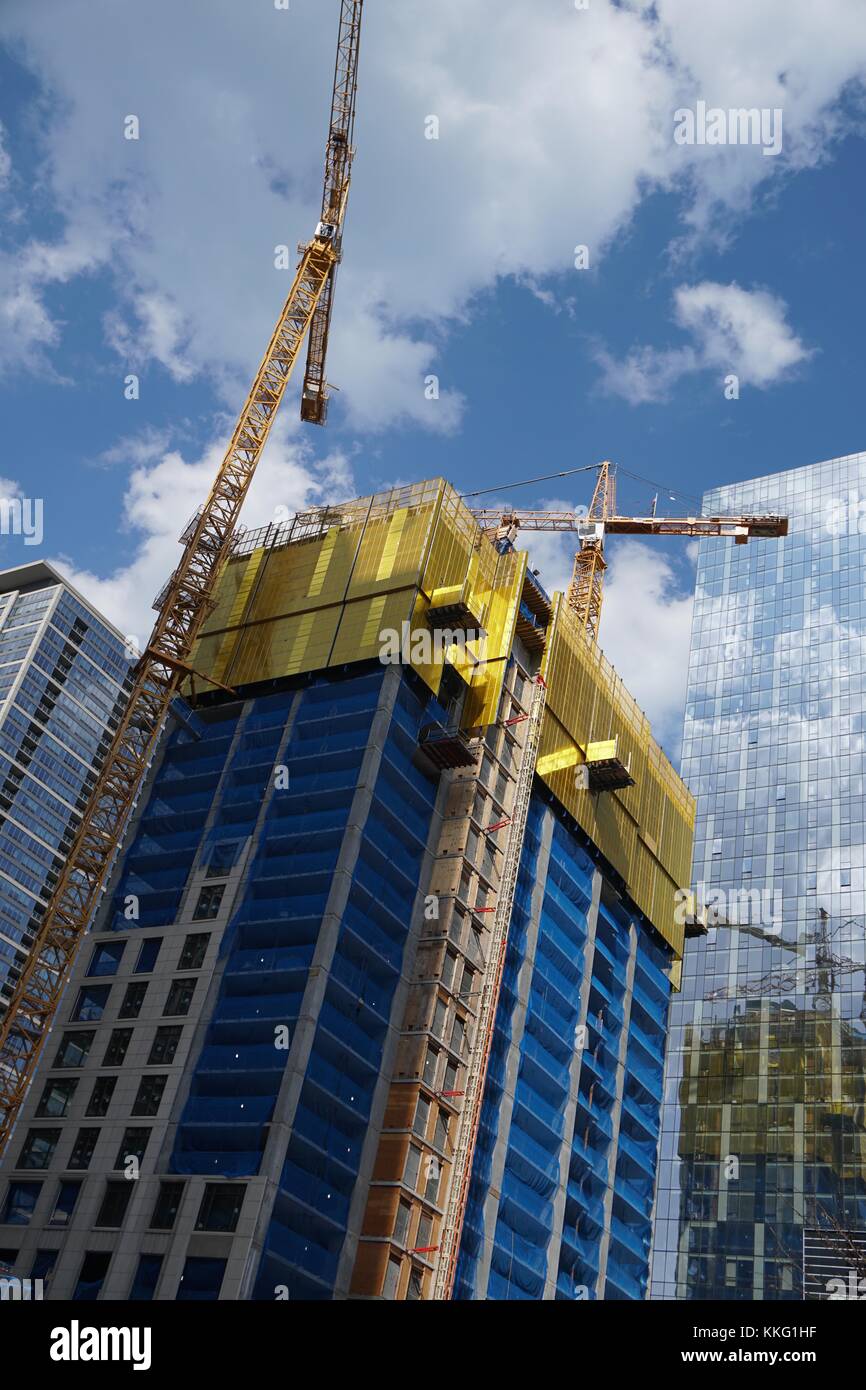 Looking up at skyscraper under construction with blue and yellow building material, yellow crane, blue sky and clouds Stock Photo