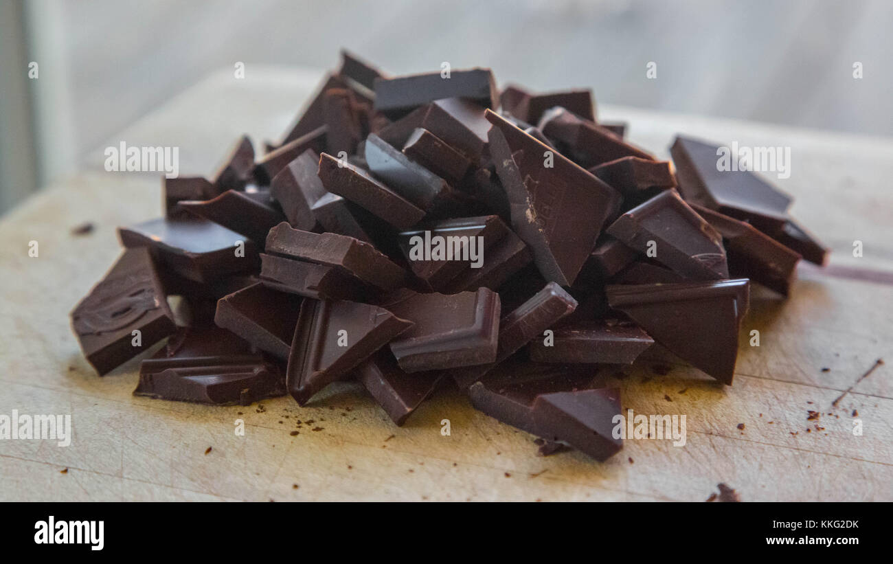 A pile of chopped chocolate sits on a wooden cutting board, ready to be baked into a dessert Stock Photo