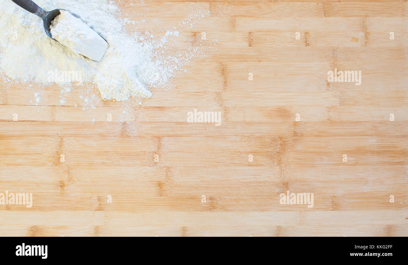 Flour sits in a metal scoop on a wooden cutting board Stock Photo
