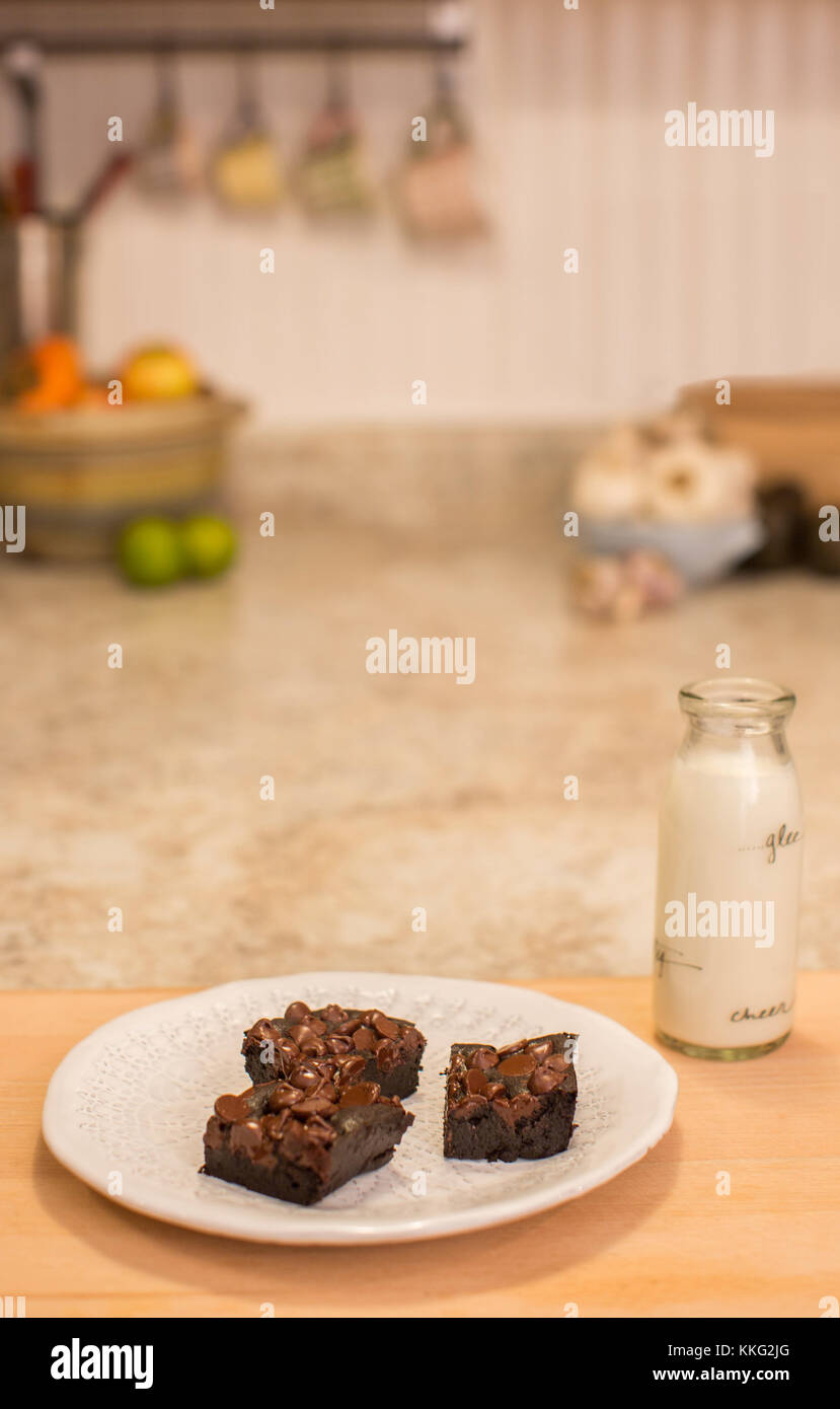 Fresh chocolate brownies sit on a plate in the kitchen with a bottle of milk Stock Photo