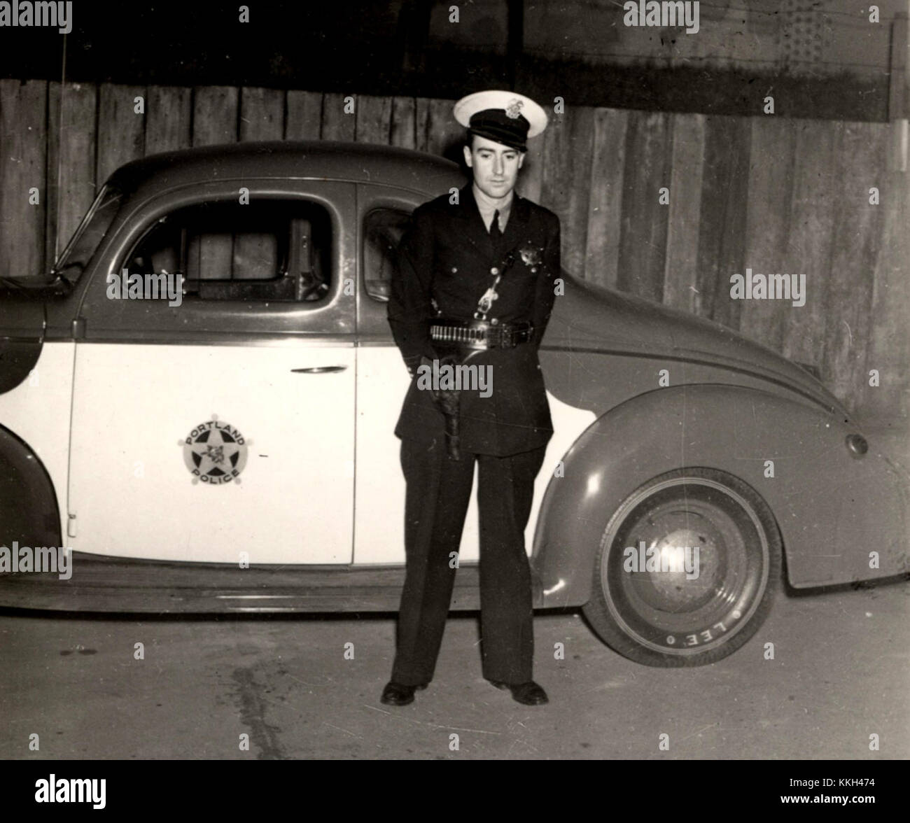 This image shows a police officer standing in front of a patrol car ...