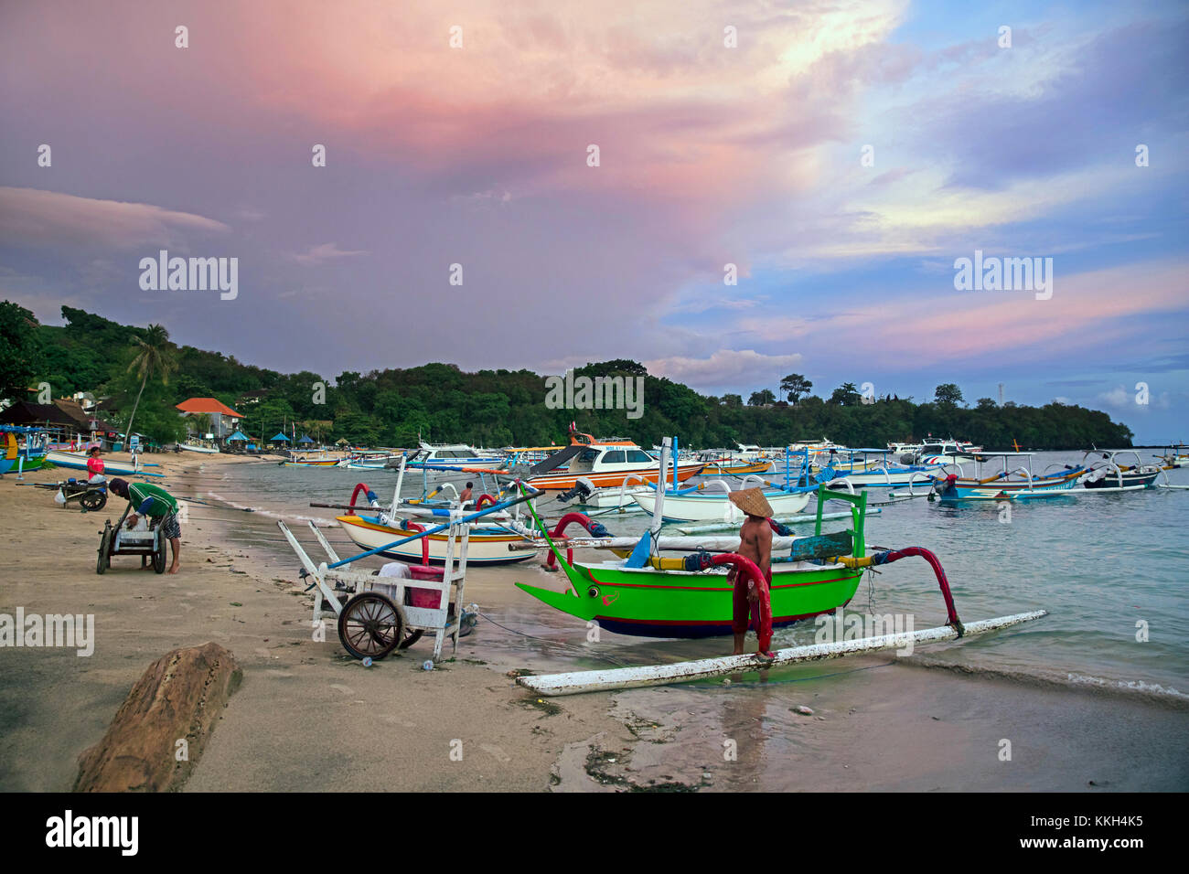 Balinese fishermen with traditional outrigger fishing boats in the bay of Padang Bai / Padangbai / Padang Bay at sunset on the island Bali, Indonesia Stock Photo