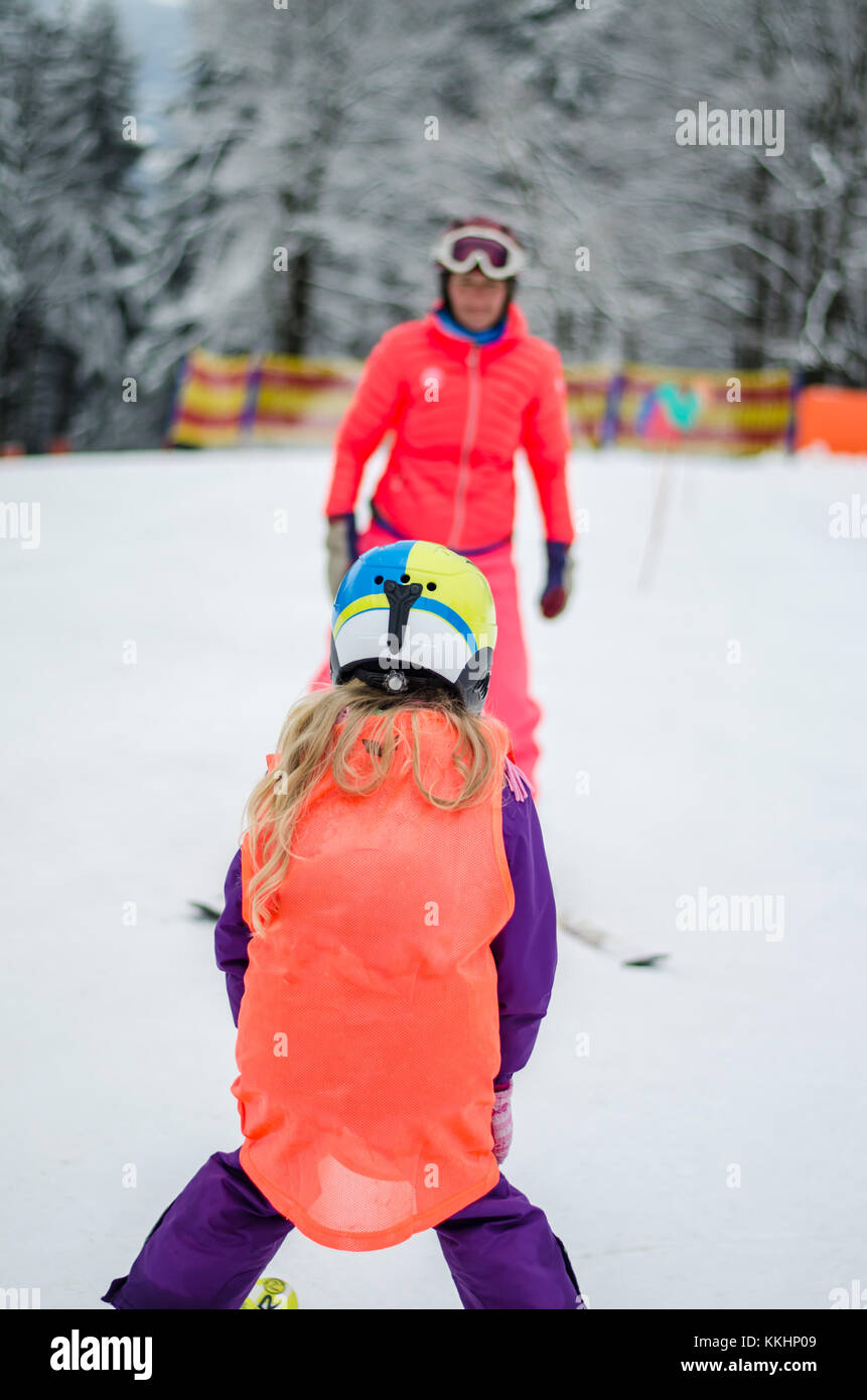 little blond girl learning to ski with skiing instructor in winter resort Stock Photo