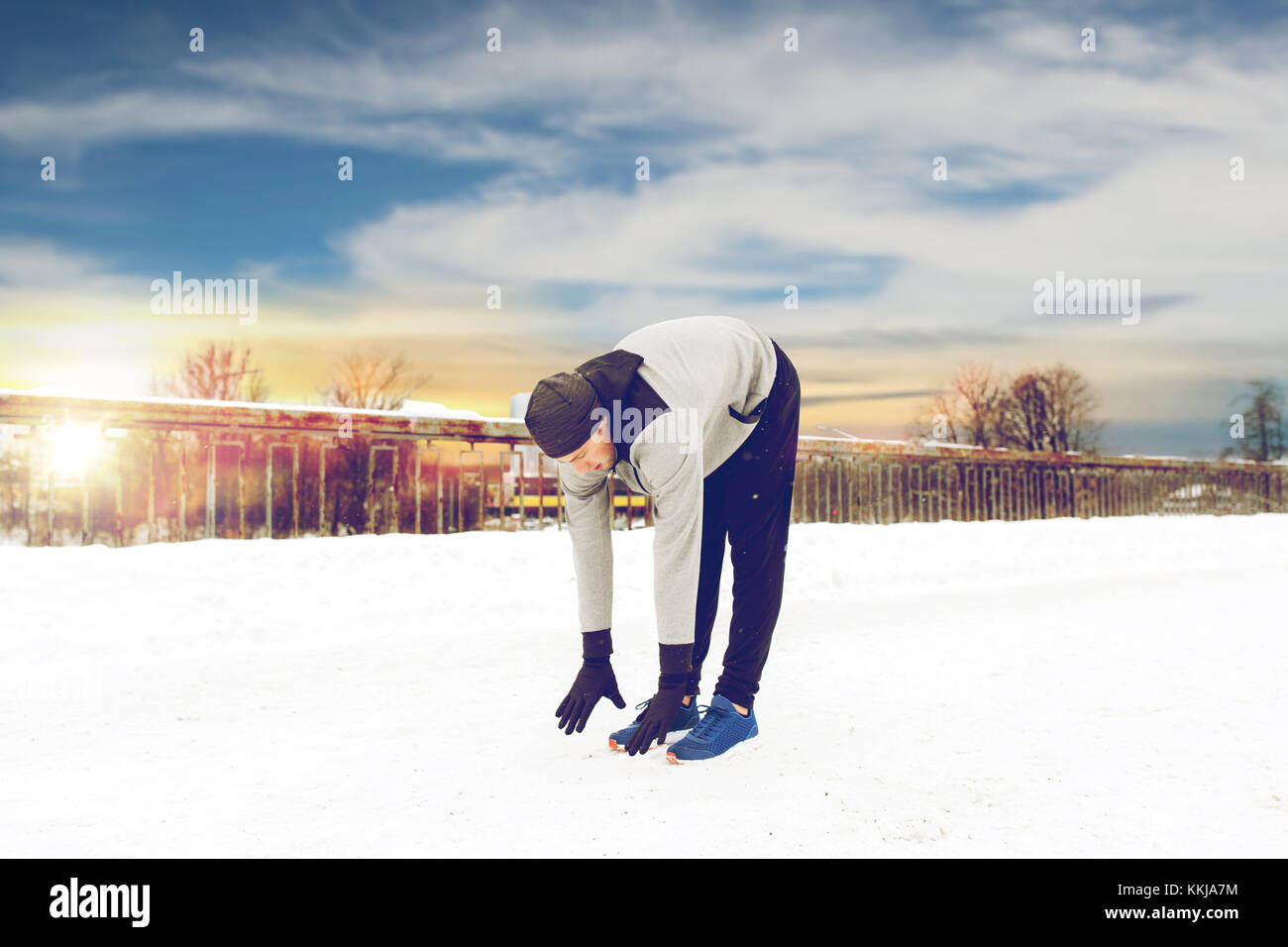 man exercising and stretching leg on winter bridge Stock Photo