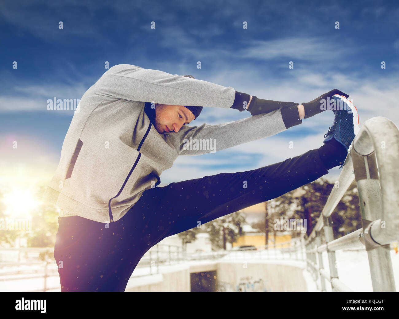 sports man stretching leg at fence in winter Stock Photo