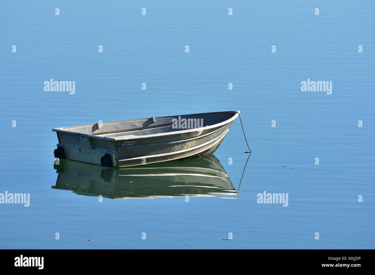 Lonely tiny tin boat reflecting on very calm blue water surface Stock