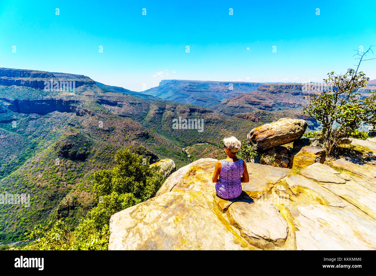 Senior woman sitting on a cliff's edge enjoying the view of the Blyde ...