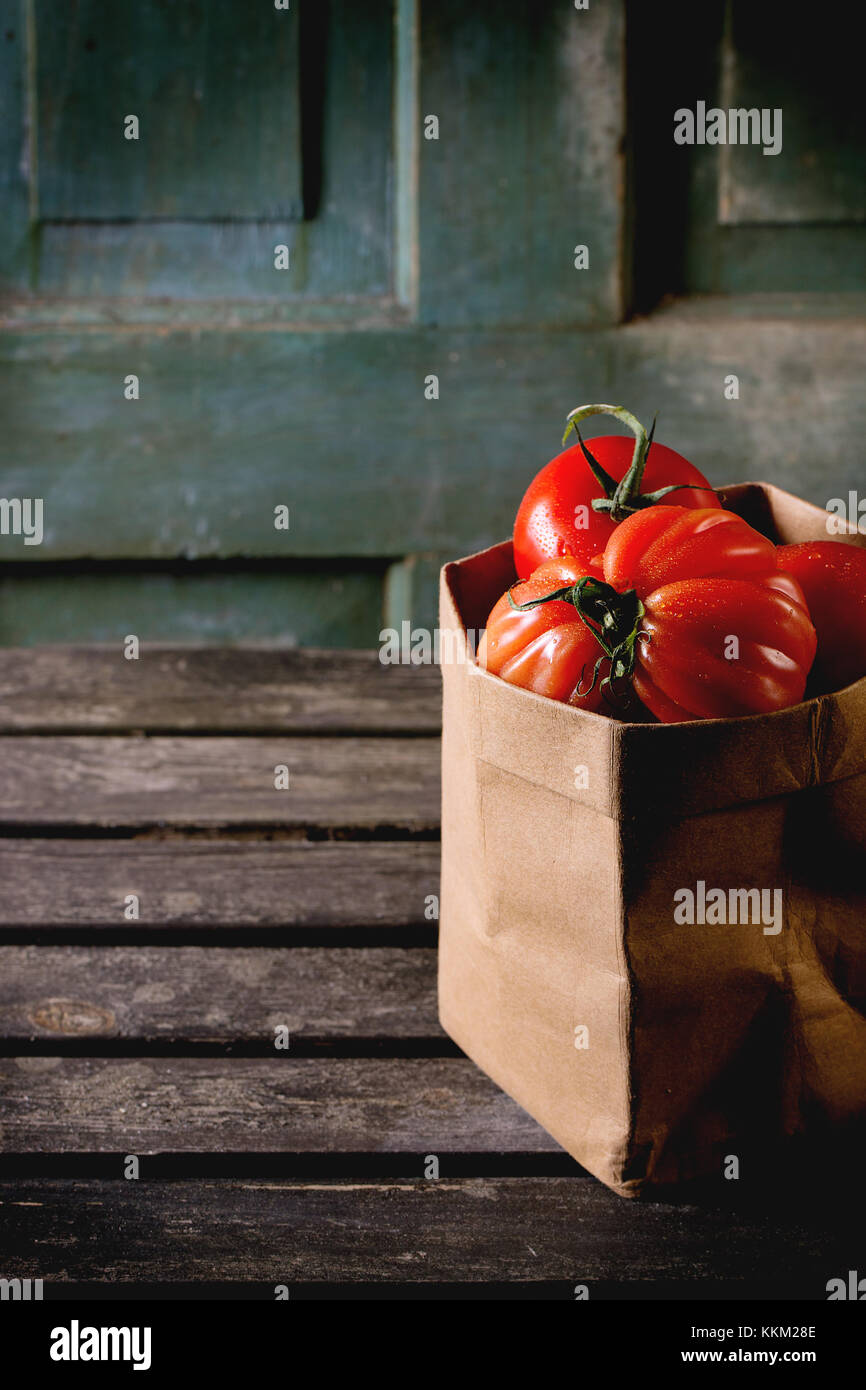 Heap of big red tomatoes RAF in paper bag over old wooden table. Dark ...