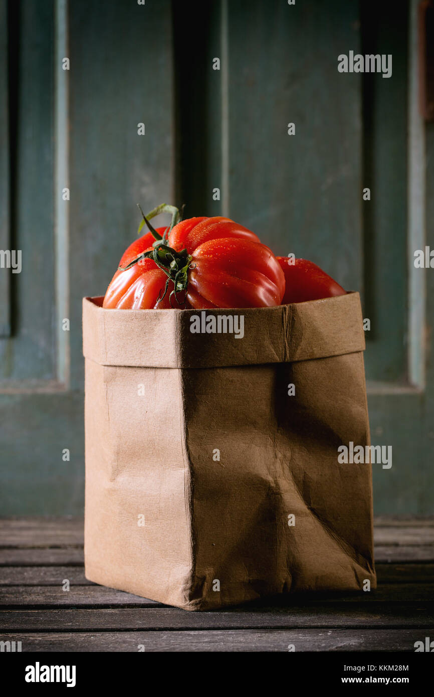 Heap of big red tomatoes RAF in paper bag over old wooden table. Dark ...