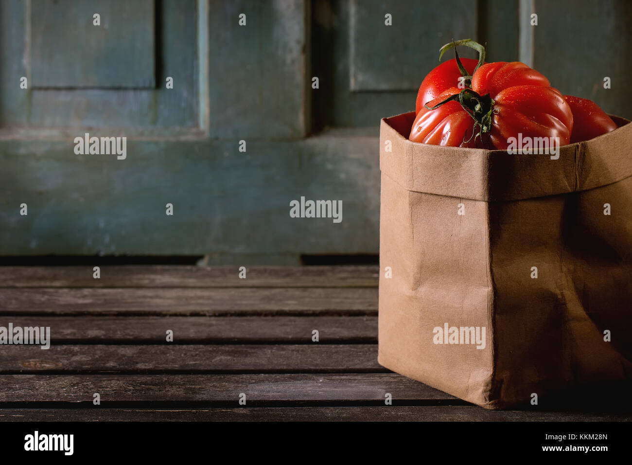 Heap of big red tomatoes RAF in paper bag over old wooden table. Dark ...
