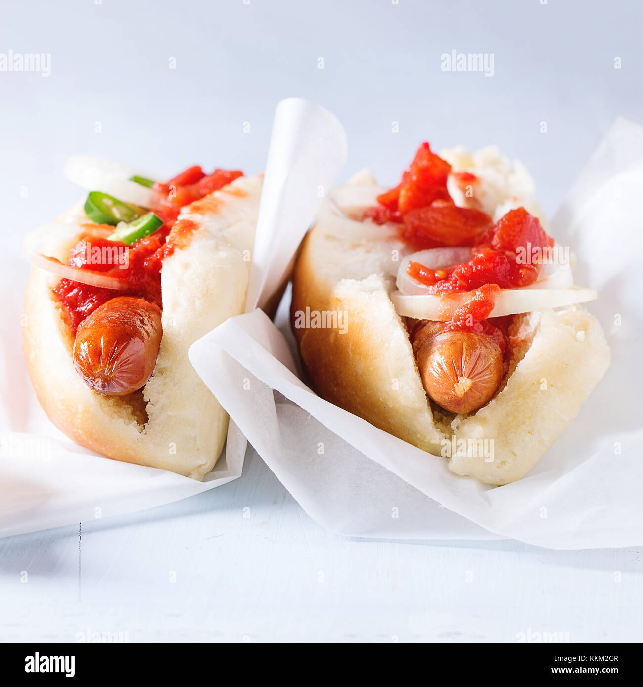 Homemade hot dogs on baking papper with tomato sauce, onion, pepper on light blue wooden background. Square image with selective focus Stock Photo