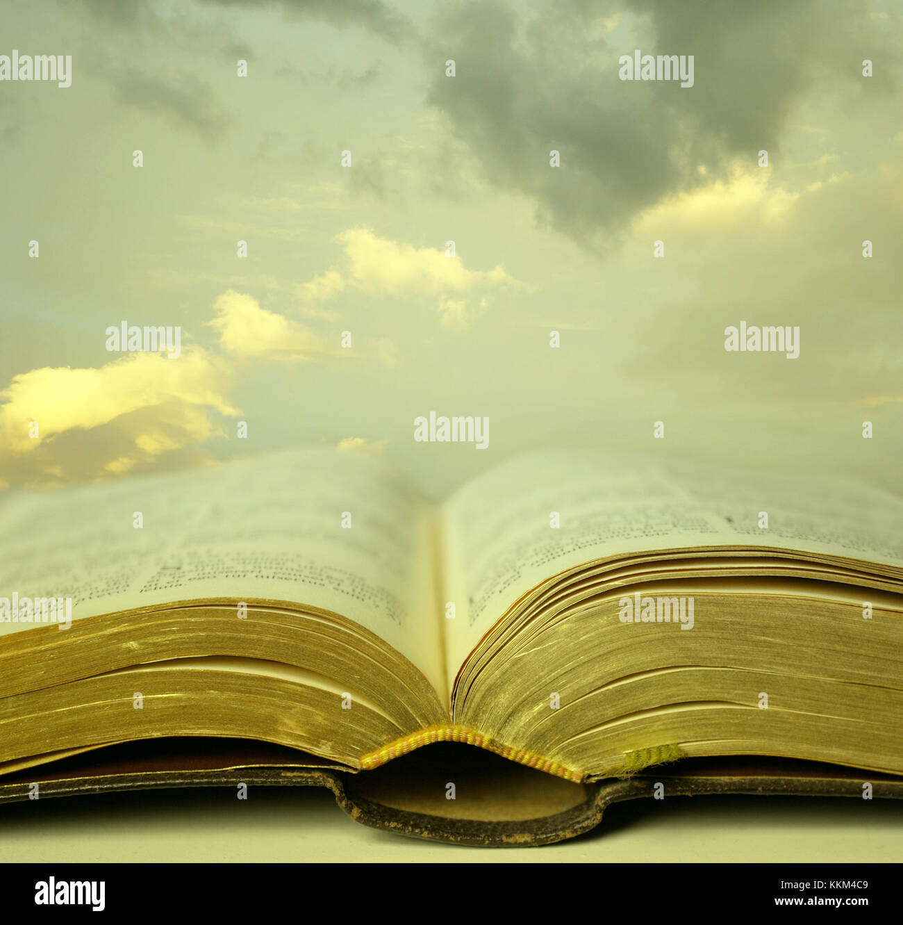 Detail of an old holy bible open with a beautiful and mystical sky in the background in a golden light Stock Photo