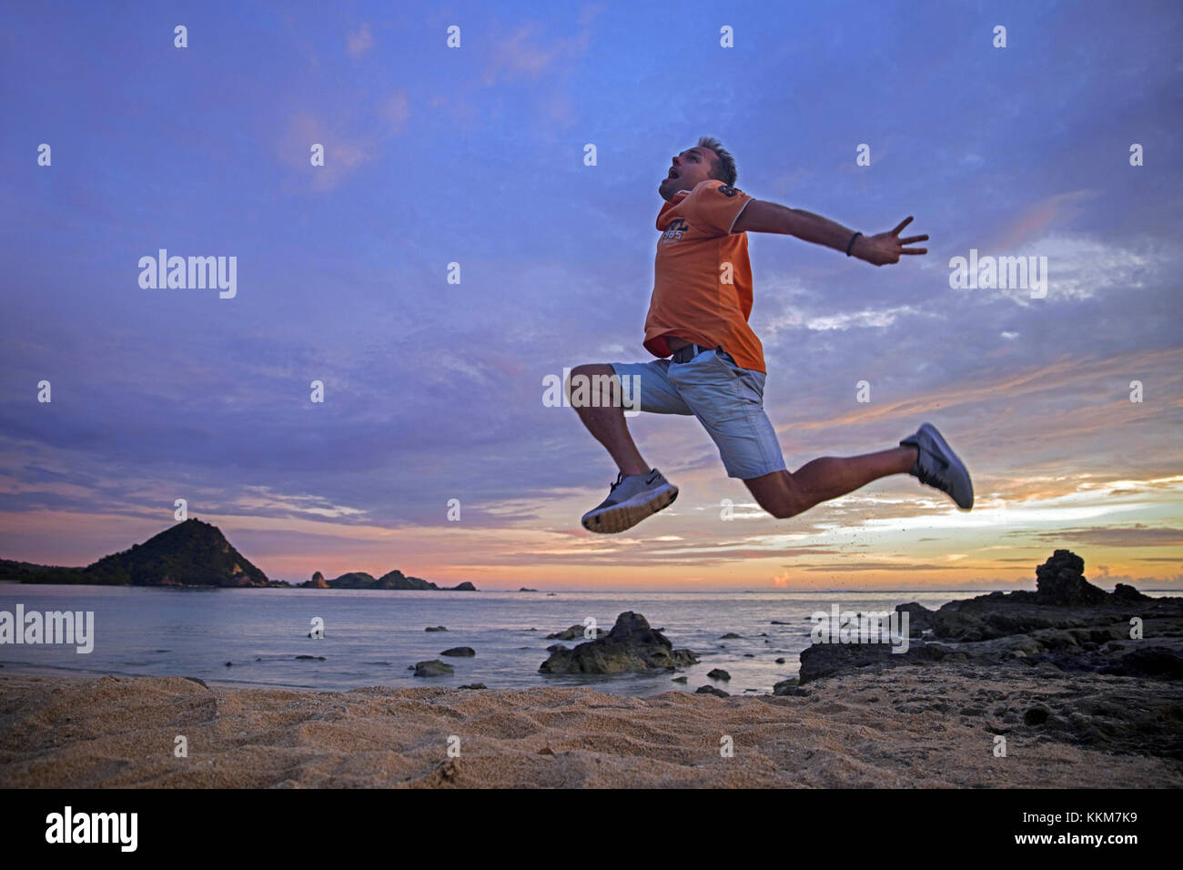 Happy Western tourist jumping in the air at sunset on the Kuta beach on the island Lombok, Lesser Sunda Islands, Indonesia Stock Photo