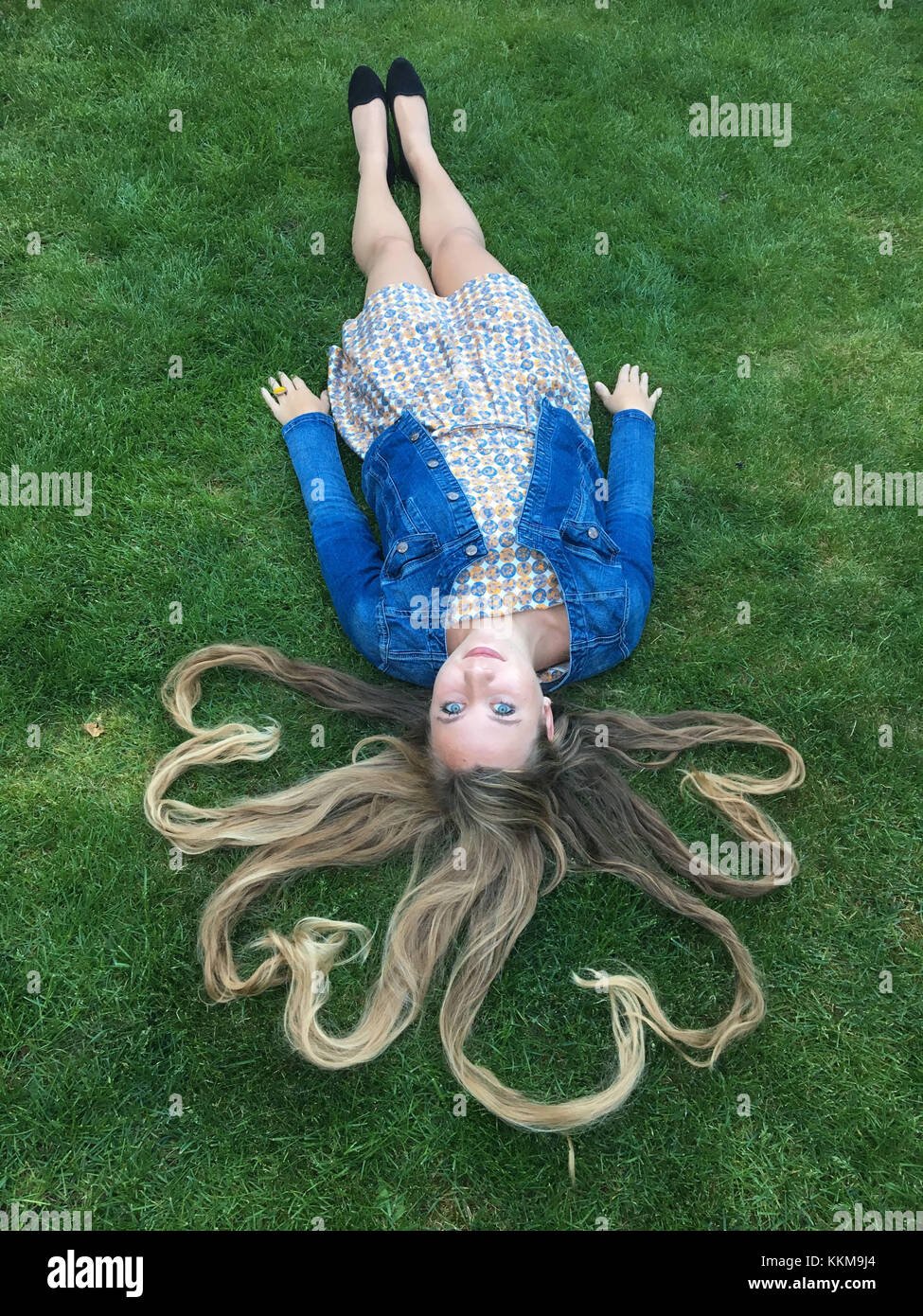 Young woman with dress and denim jacket lying in a meadow, hair in heart-shape Stock Photo