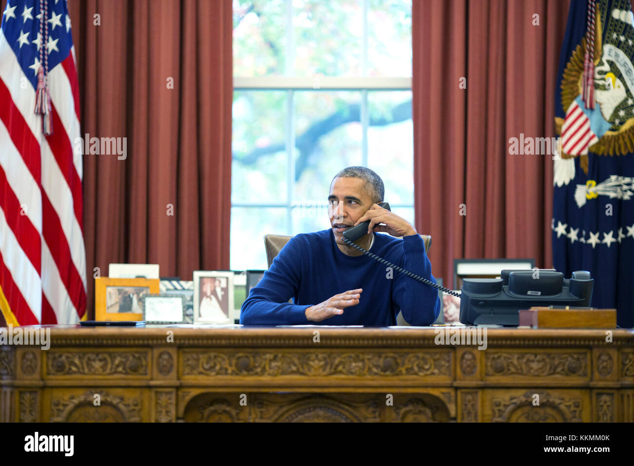 President Barack Obama makes Thanksgiving Day phone calls from the Oval Office to U.S. troops stationed around the world, Nov. 24, 2016. The President's Coast Guard military aide, LCDR Ginny Nadolny is at right. (Official White House Photo by Pete Souza) Stock Photo