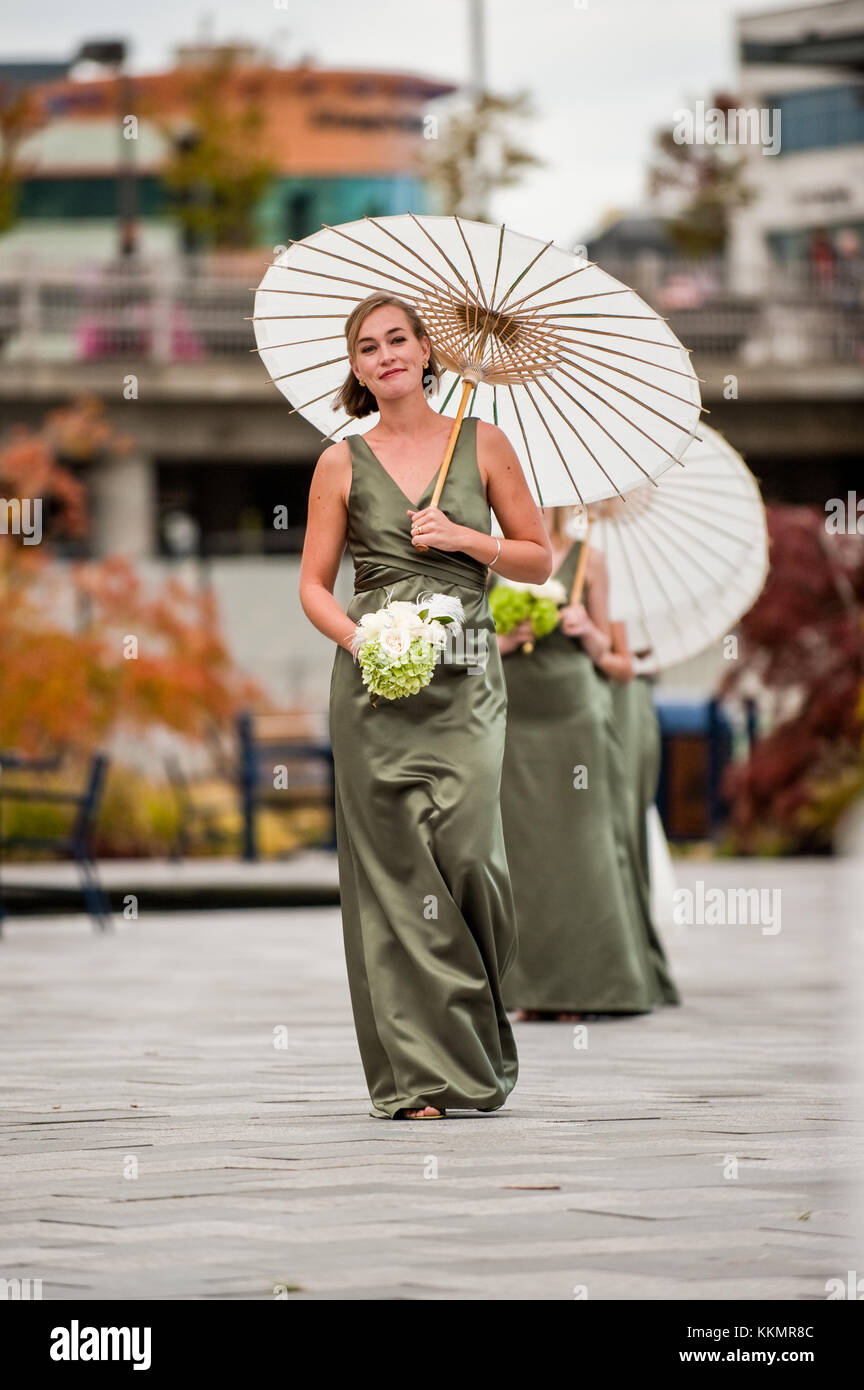 Bridesmaids in green dresses and oriental umbrella walking down the park at wedding ceremony at Harborside Fountain Park at Bremerton ferry terminal Stock Photo