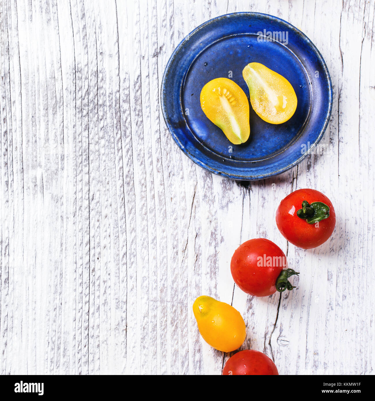 Blue ceramic plate with mix of red and yellow cherry tomatoes over white wooden table. Top view. Square image Stock Photo