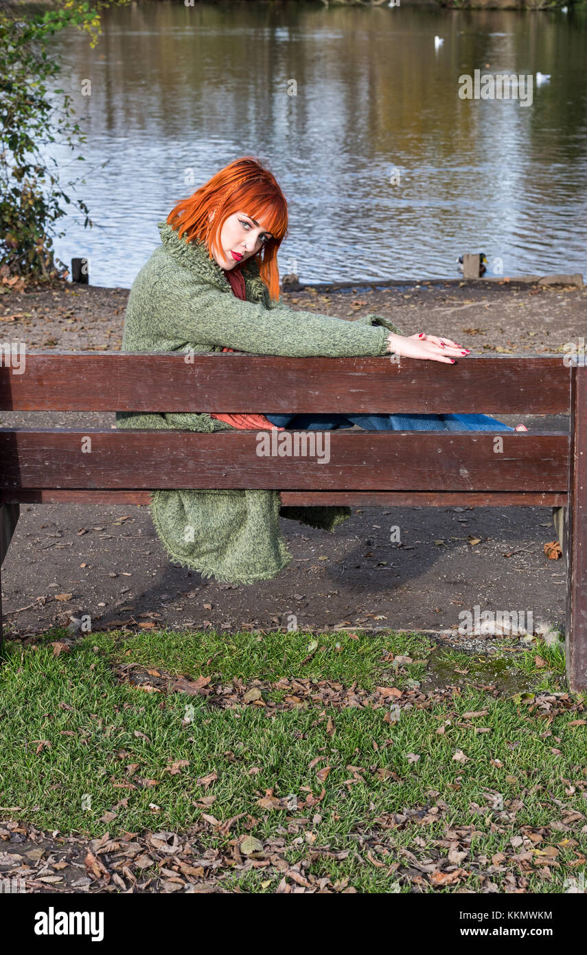 Redhead Girl on bench in park in autumn Stock Photo