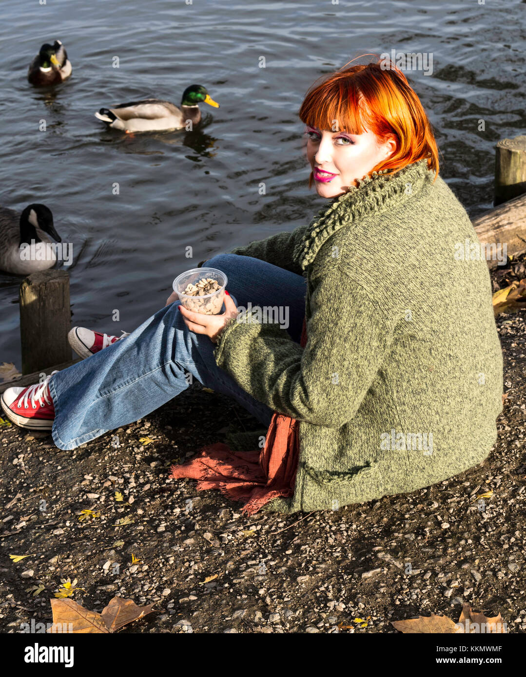 Beautiful girl in park feeding ducks in fall Stock Photo