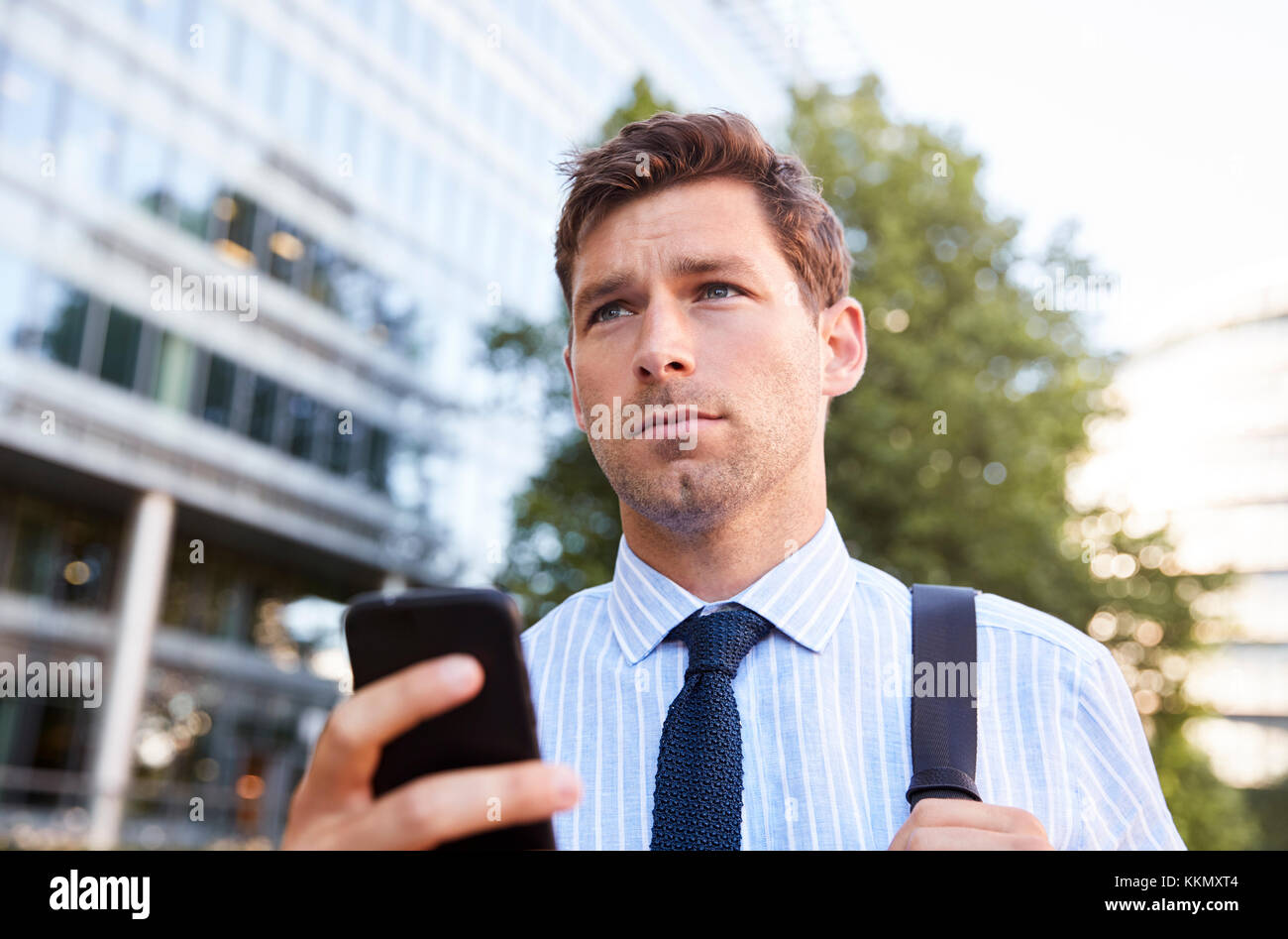 Businessman Walking To Work In City Looking At Mobile Phone Stock Photo