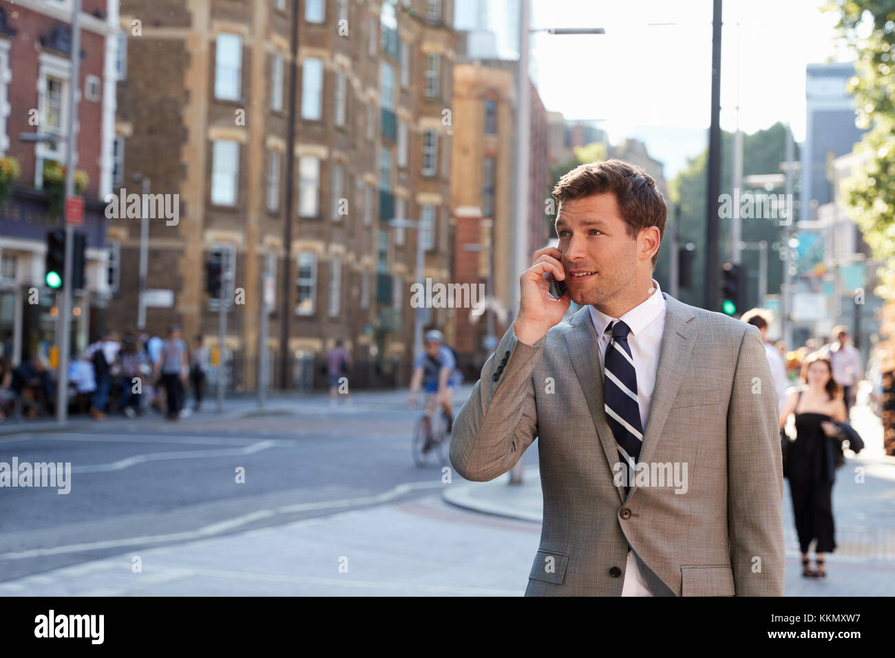 Businessman Talking On Mobile Phone Walking Along City Street Stock Photo
