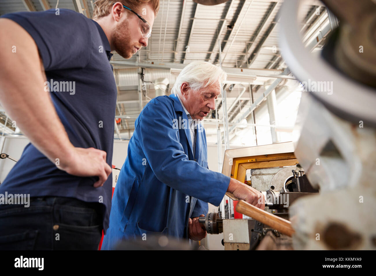 Senior engineer demonstrating equipment to apprentice at machine bench, low angle Stock Photo