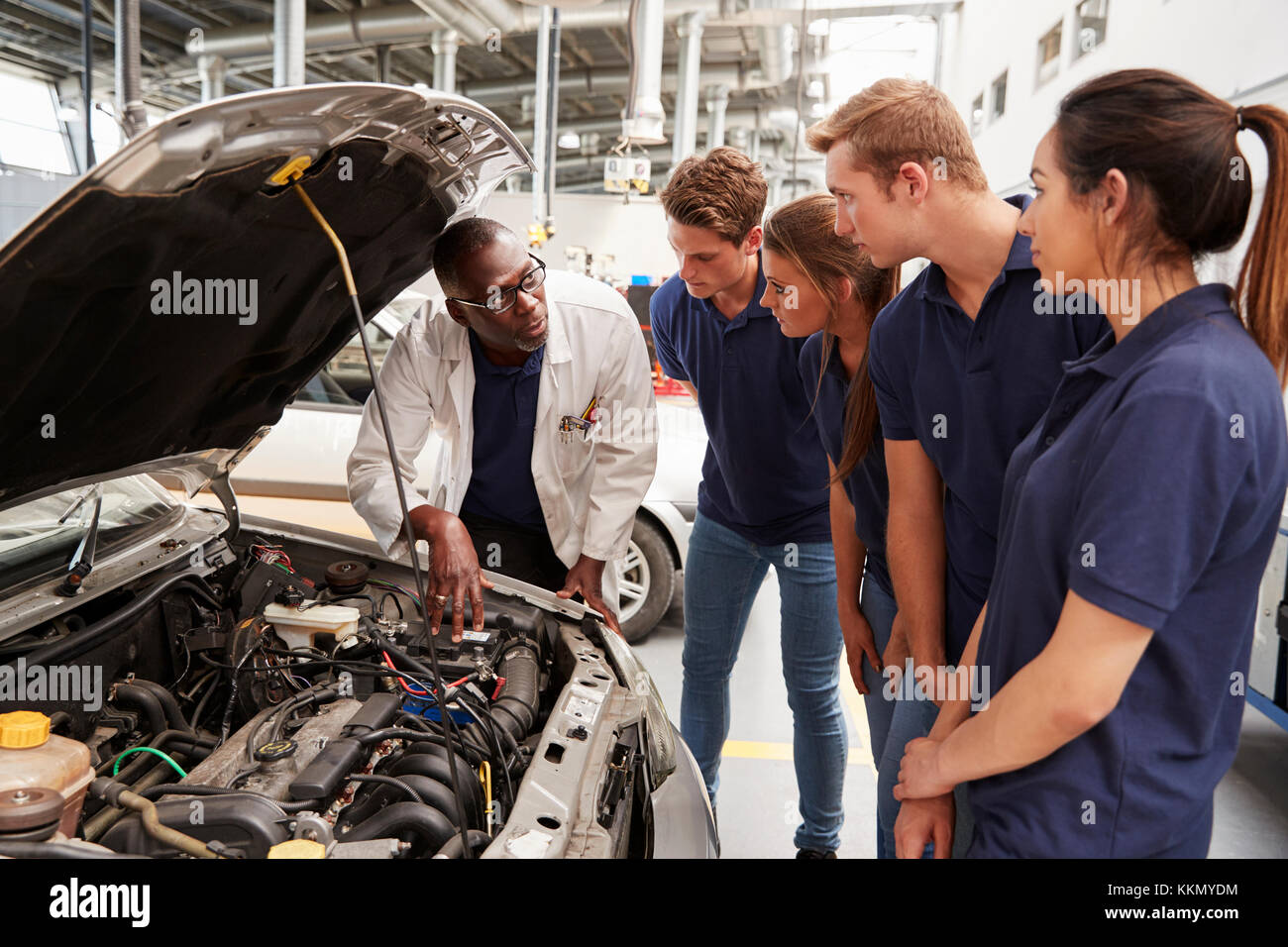Mechanic instructing trainees around the engine of a car Stock Photo