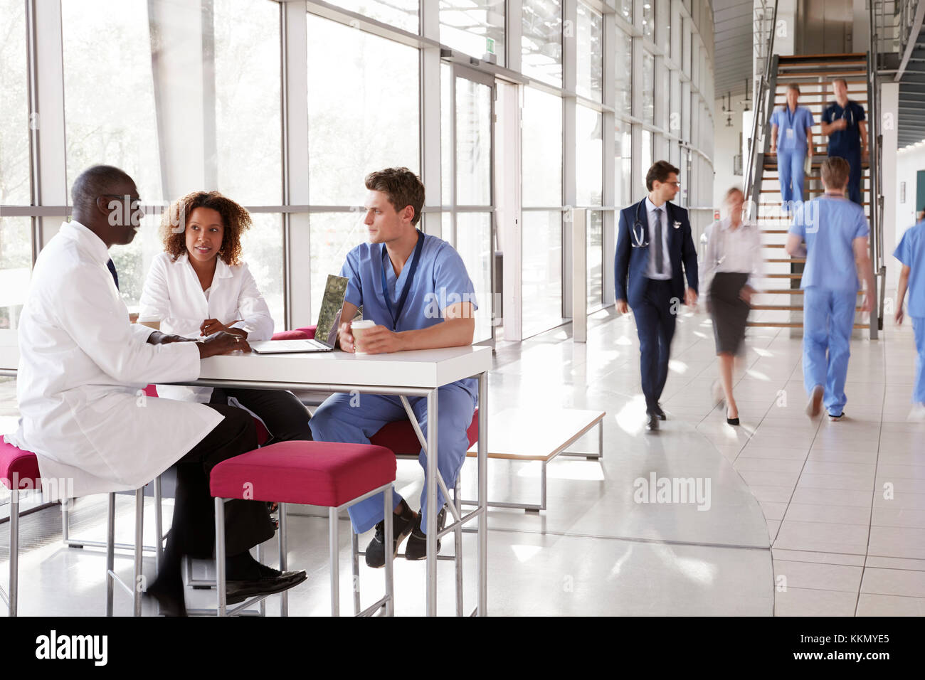 Three healthcare workers talking in a busy modern lobby Stock Photo Alamy