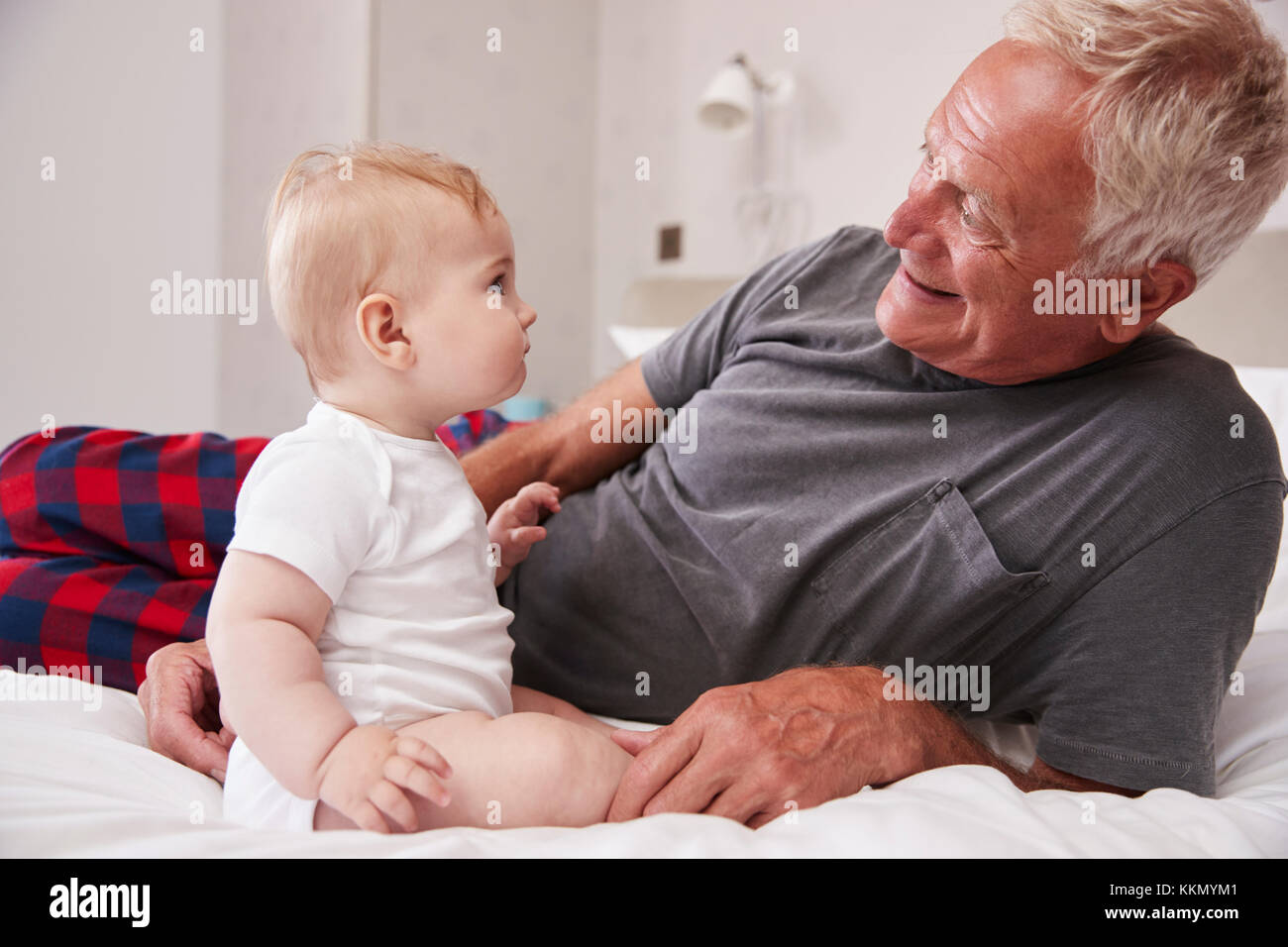 Grandfather Lying In Bed At Home Looking After Baby Grandson Stock Photo