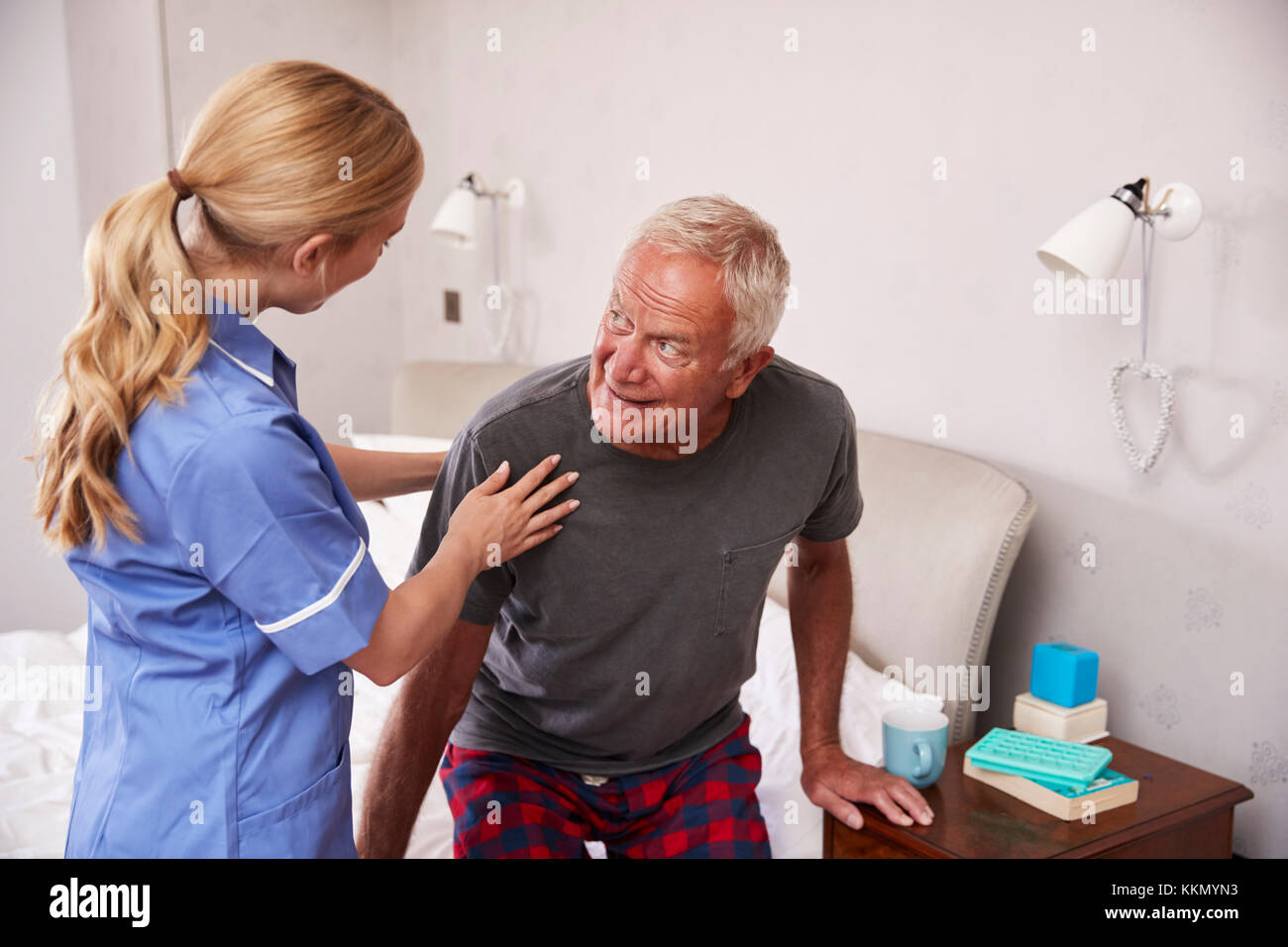 Nurse Helping Senior Man Out Of Bed On Home Visit Stock Photo